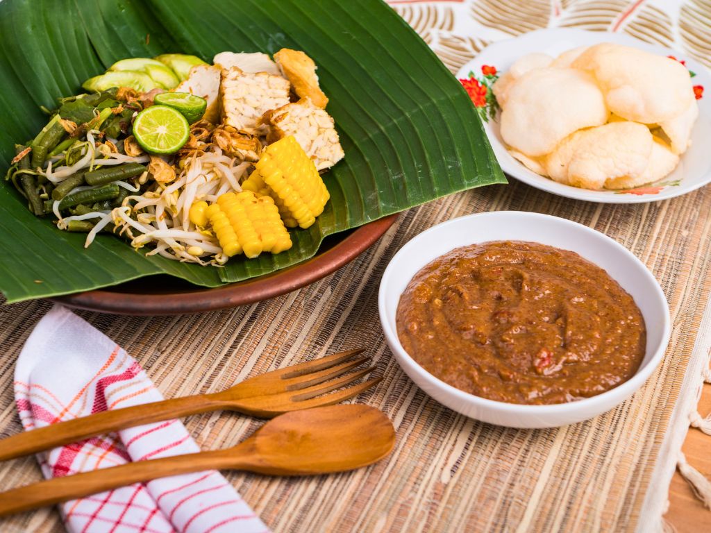 gado gado indonesian dish on a banana leaf with crackers and peanut sauce on the side