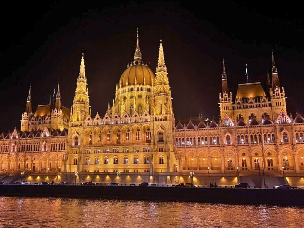 hungarian parliament building lit up at night as seen from the river