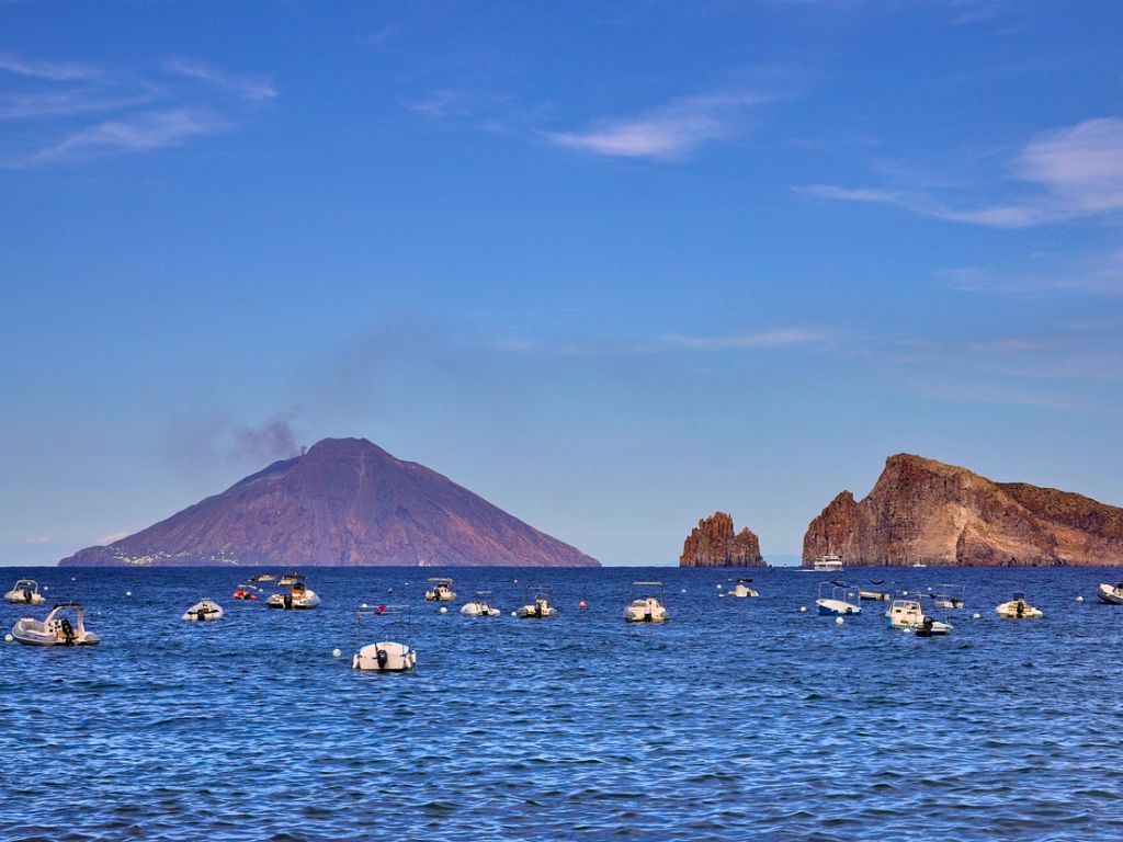 view of stromboli of the aeolian islands from the sea with other rocks and boats on the water